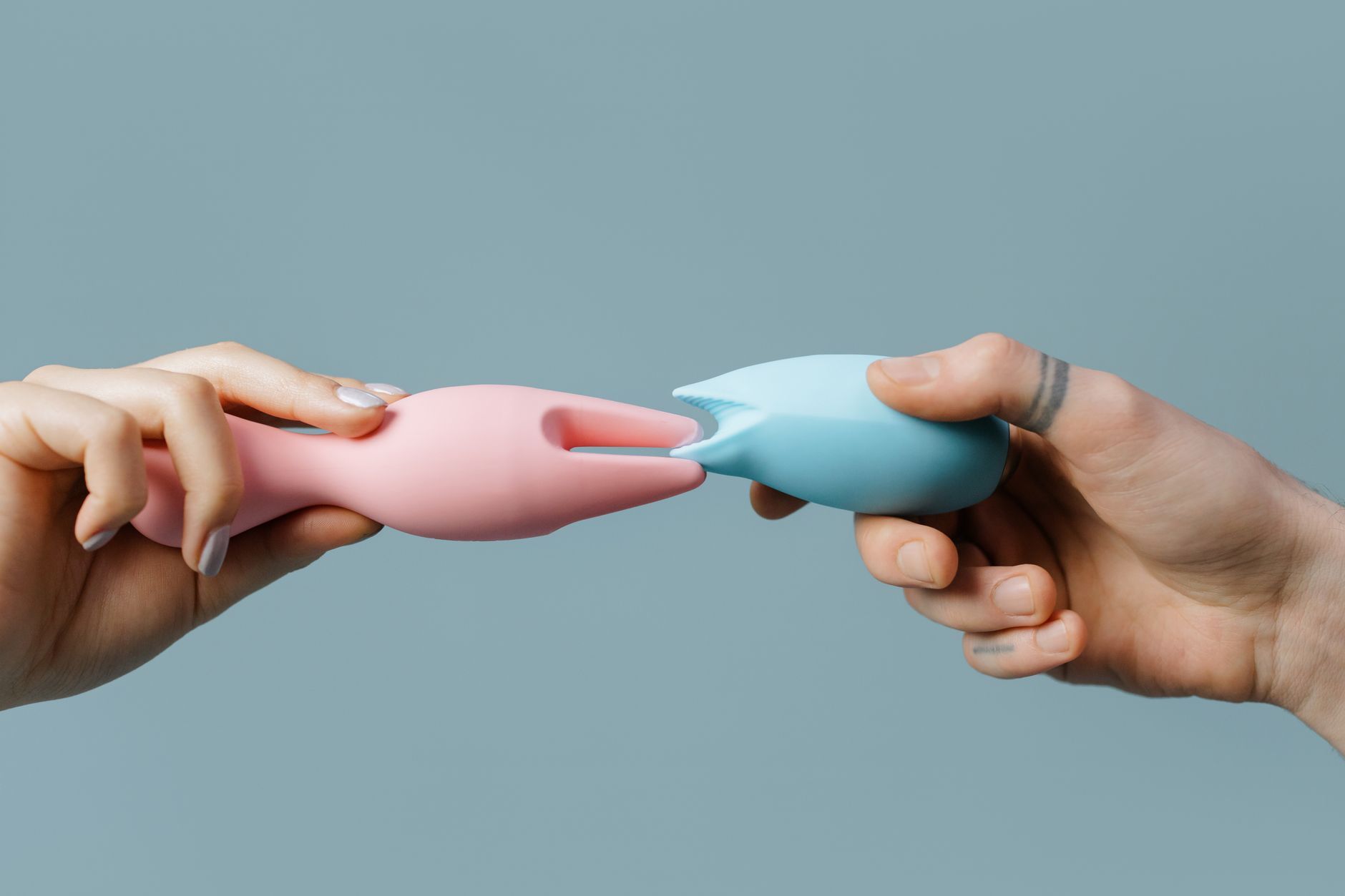 Hands holding pastel-colored clitoral vibrators on a neutral background