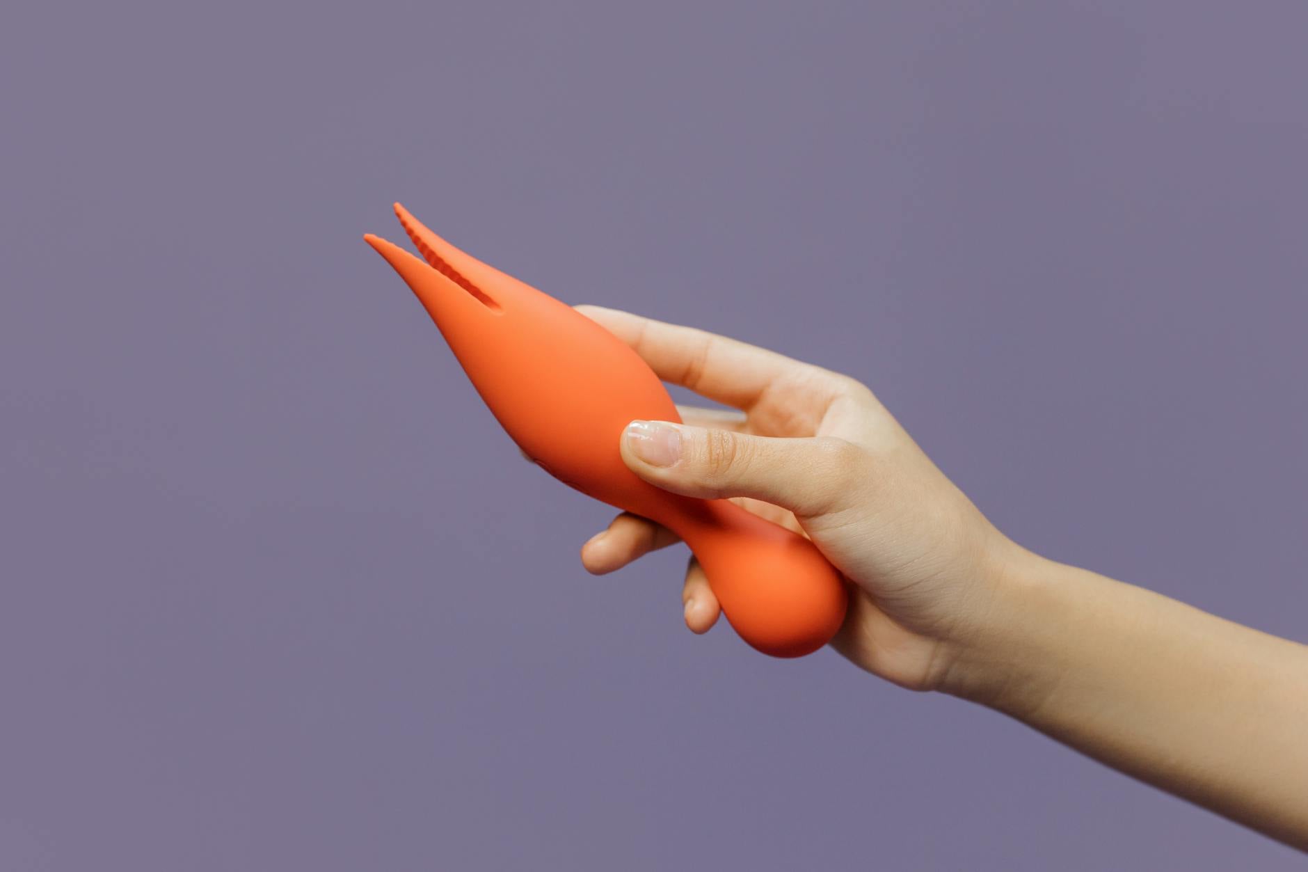 Close-up of a hand holding a lemon vibrator against a minimalistic purple backdrop, showcasing modern sensuality.