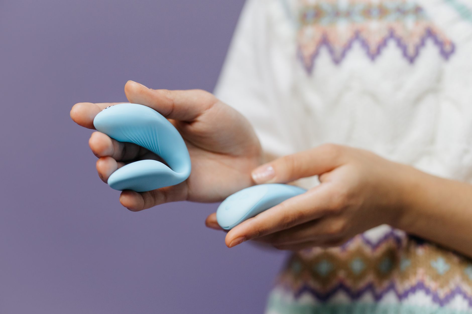 Close-up of hands holding a sleek blue vibrator against a purple background, representing safe and intentional pleasure.