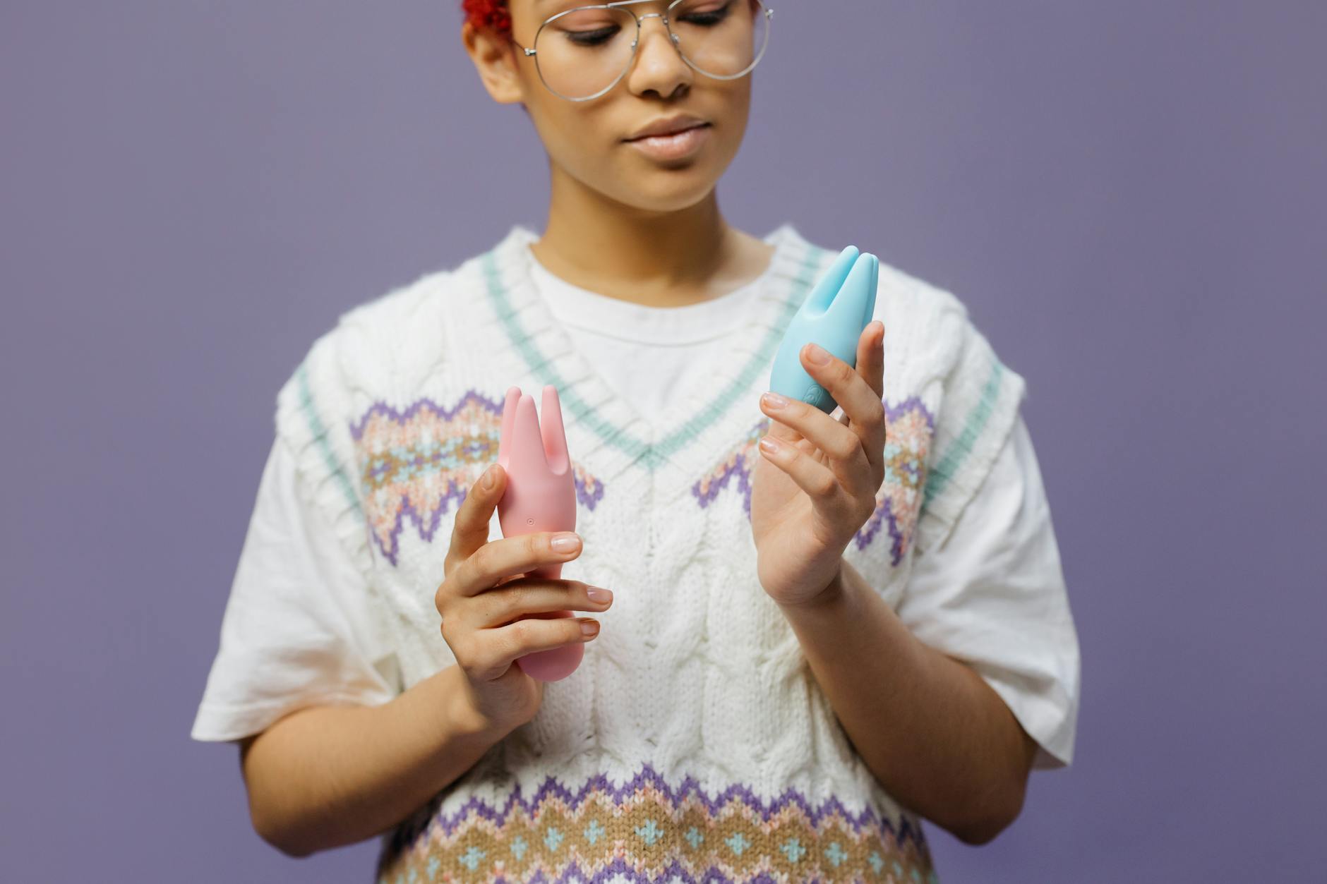 Woman holding lemon and pink silicone clitoral vibrators in contemplative pose