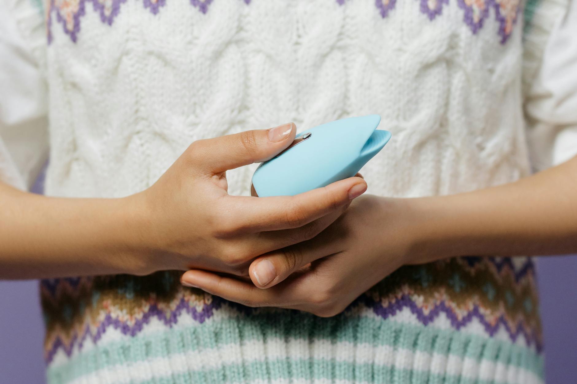 Woman holding blue vibrator against knitted sweater